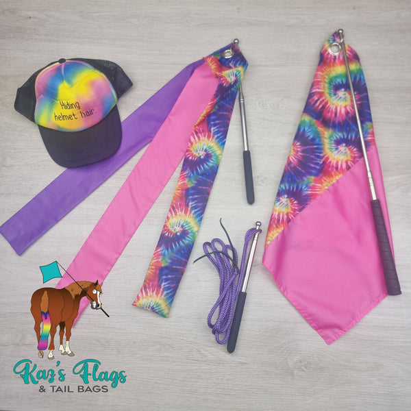 Colorful tie-dye flags and a cap on a gray surface with 'Kaz's Flags & Tail Bags' branding.