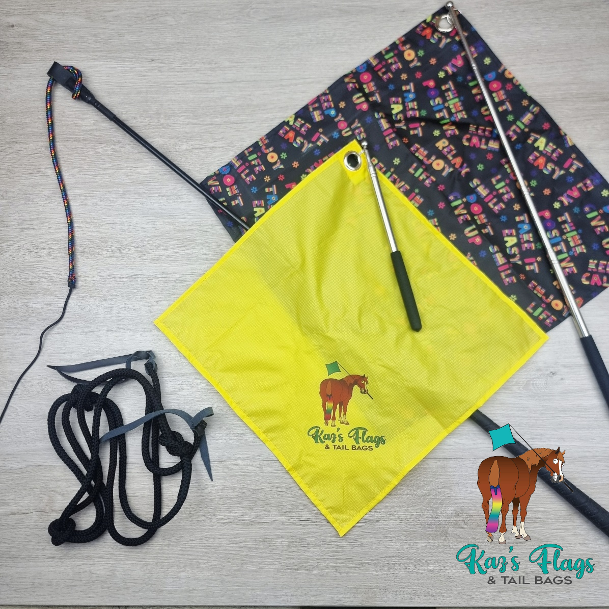 A flat-lay product display of a horse flag set on a light gray wood floor. The set includes a bright yellow square flag with a printed brown horse logo and the text 'Kaz's Flags & Tail Bags', a black and multicolor patterned rectangular flag, black poles with silver metal sections, black neck rope.