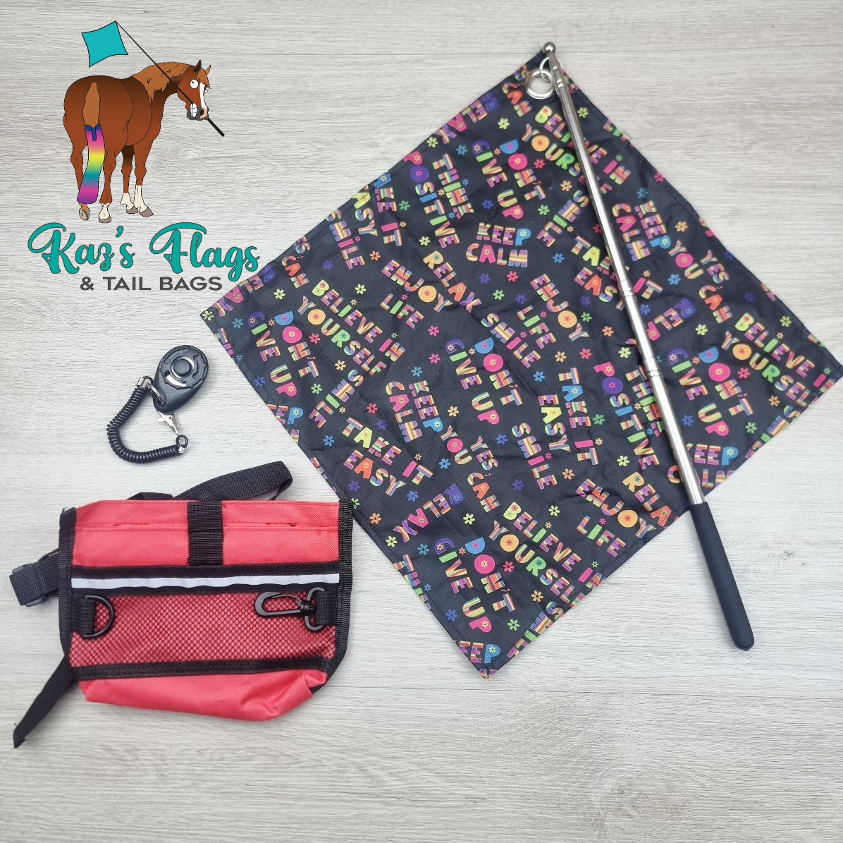 A flat-lay product photo of a horse riding flag set by Kaz's Flags & Tail Bags, featuring a black flag with colorful text and a horse illustration, a red and black treat pouch bag, and a black clicker. The background is a light gray wood floor.