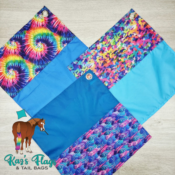 Colorful horse flags with tie-dye, butterfly, and feather patterns on a wooden surface.