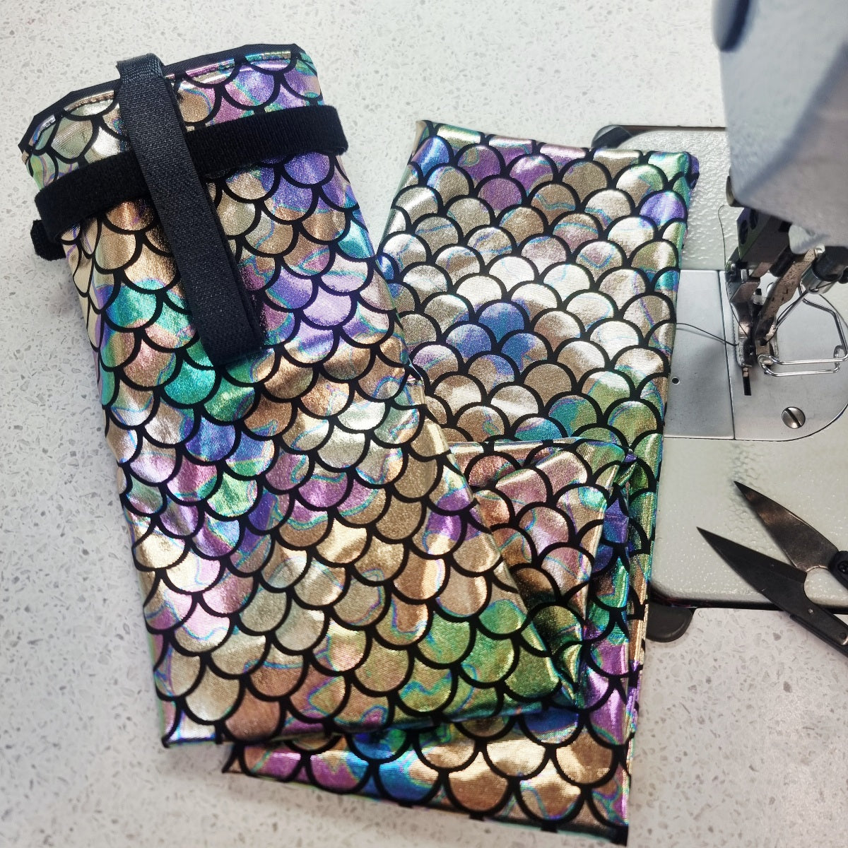 Multicolored fish-scale patterned tail bag with a black strap on a light gray surface.