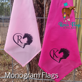 Two monogram horse training flags hanging on a wire fence outdoors. One flag is light pink with a black horse silhouette and letter 'R' inside a heart.