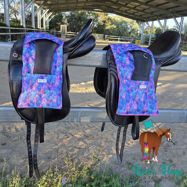 Two horse saddles with colorful stirrup and girth covers on a metal railing outdoors.
