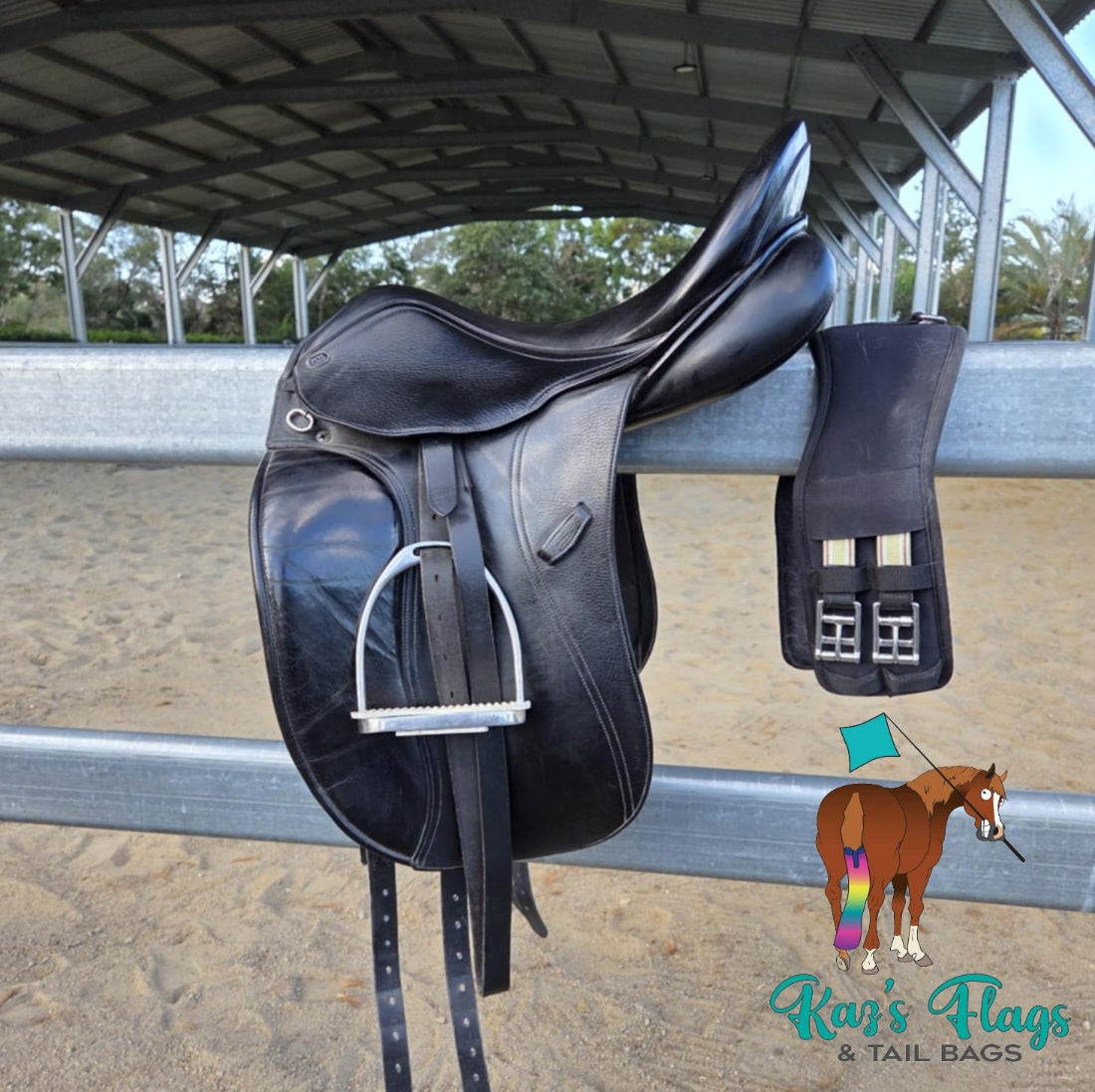 Black leather saddle with a matching black leather pad on a metal railing, with 'Kaz's Flags & Tail Bags' logo in the corner.